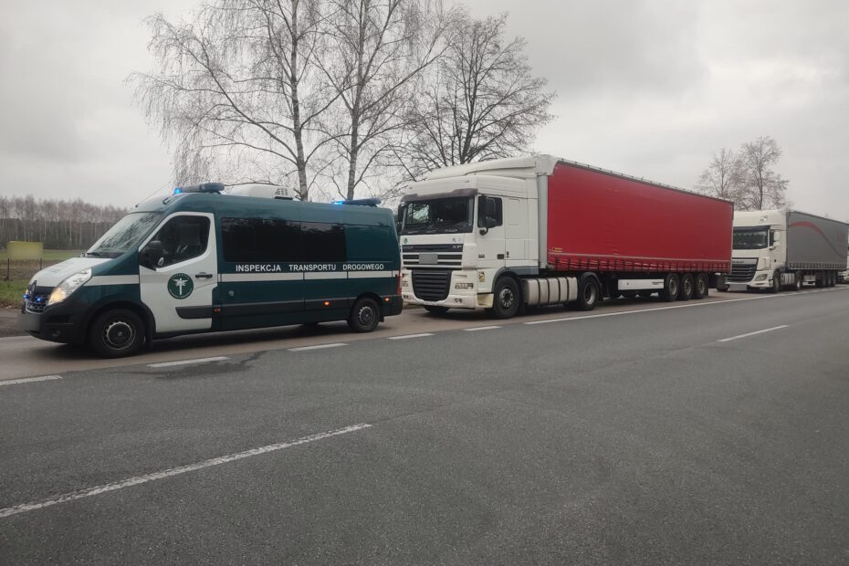 Na zdjęciu widoczny jest samochód INSPEKCJI TRANSPORTU DROGOWEGO’ oraz 2 duże ciężarówki zaparkowane na poboczu drogi. W tle widać szare niebo i bezlistne drzewa, co sugeruje pochmurny dzie