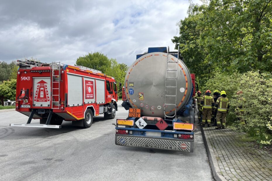 Strażacy przy cysternie i wozie strażackim podczas akcji na drodze.