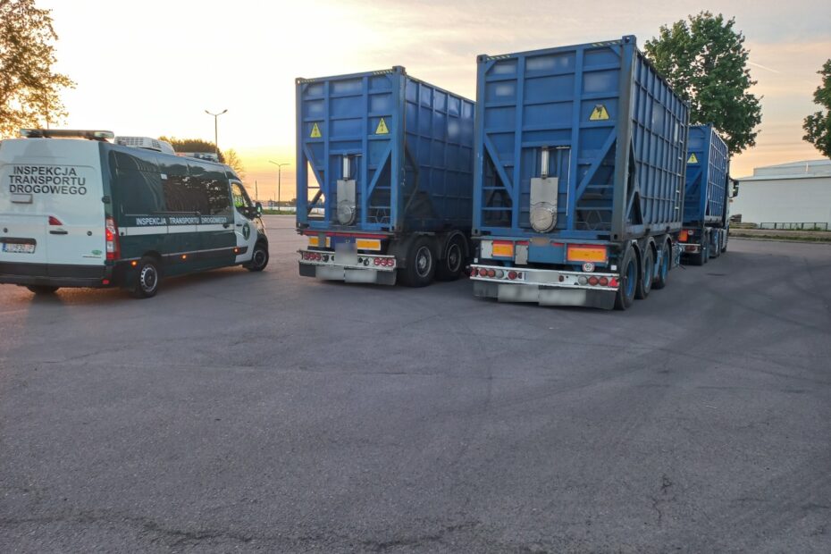 Na zdjęciu widoczne są dwa niebieskie samochody ciężarowe oraz biały pojazd Inspekcji Transportu Drogowego zaparkowane na placu asfaltowym o zachodzie słońca.