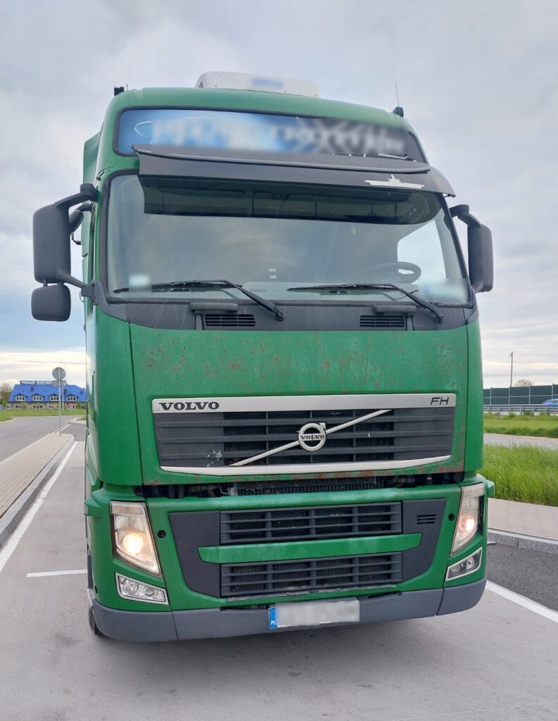 Zielona ciężarówka marki Volvo FH stoi zaparkowana na poboczu drogi. Widok jest od przodu