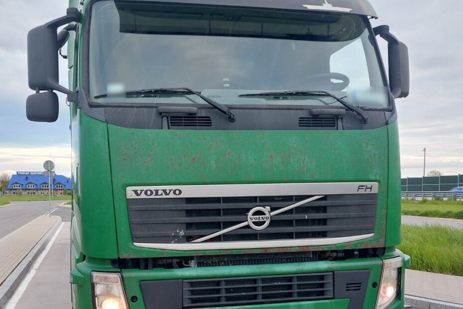 Zielona ciężarówka marki Volvo FH stoi zaparkowana na poboczu drogi. Widok jest od przodu