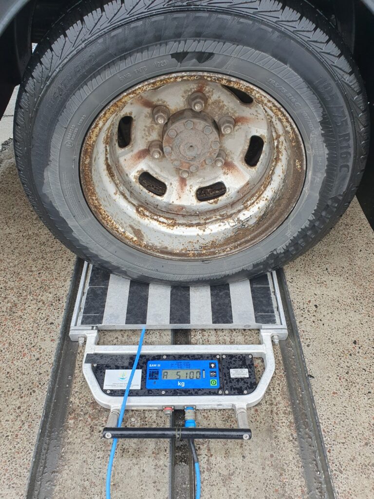 Zbliżenie na koło samochodu dostawczego ustawionego na wadze, wyświetlacz pokazuje 5100 kg