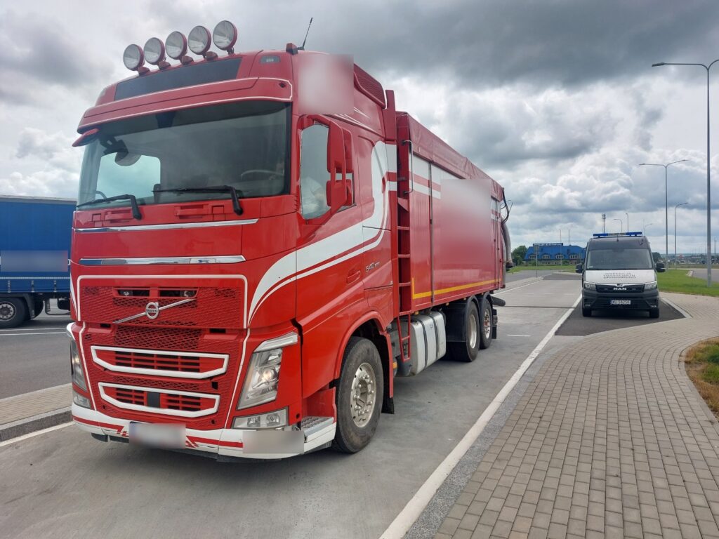 Czerwony samochód ciężarowy Volvo zaparkowany na poboczu drogi, w tle pojazd służb drogowych
