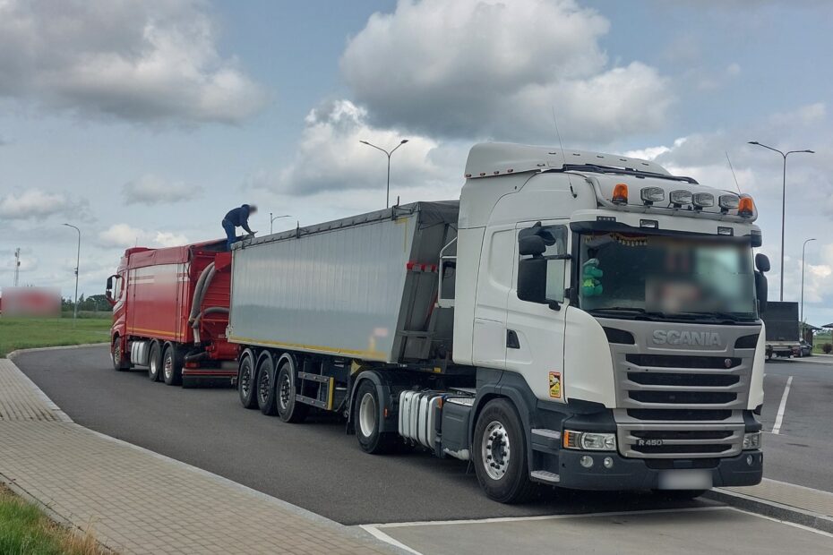 Biała ciężarówka Scania z naczepą, obok czerwony samochód ciężarowy i osoba stojąca na naczepie
