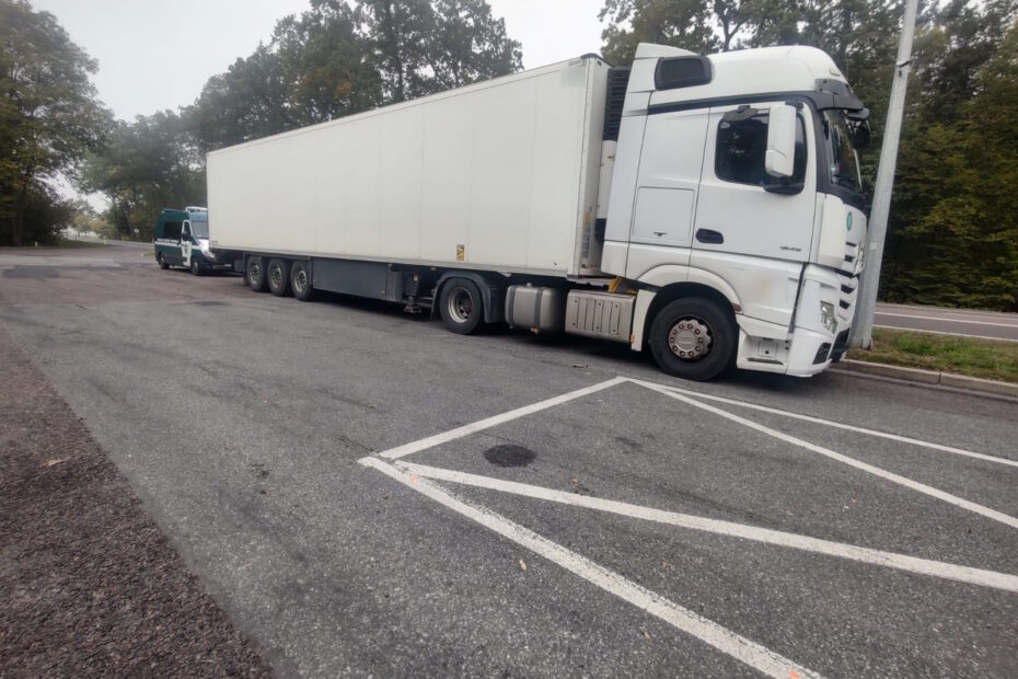 Biała ciężarówka z naczepą chłodnią zaparkowana na parkingu przy drodze.