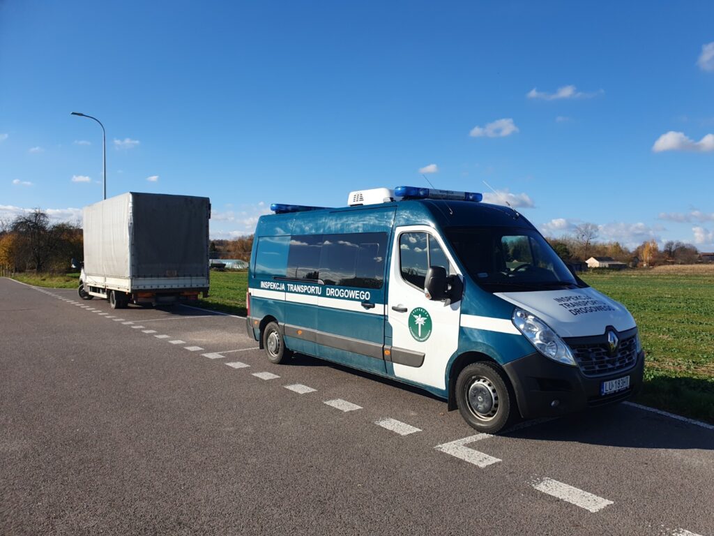 Pojazd Inspekcji Transportu Drogowego zatrzymał dostawczy samochód na poboczu drogi w słoneczny dzień.