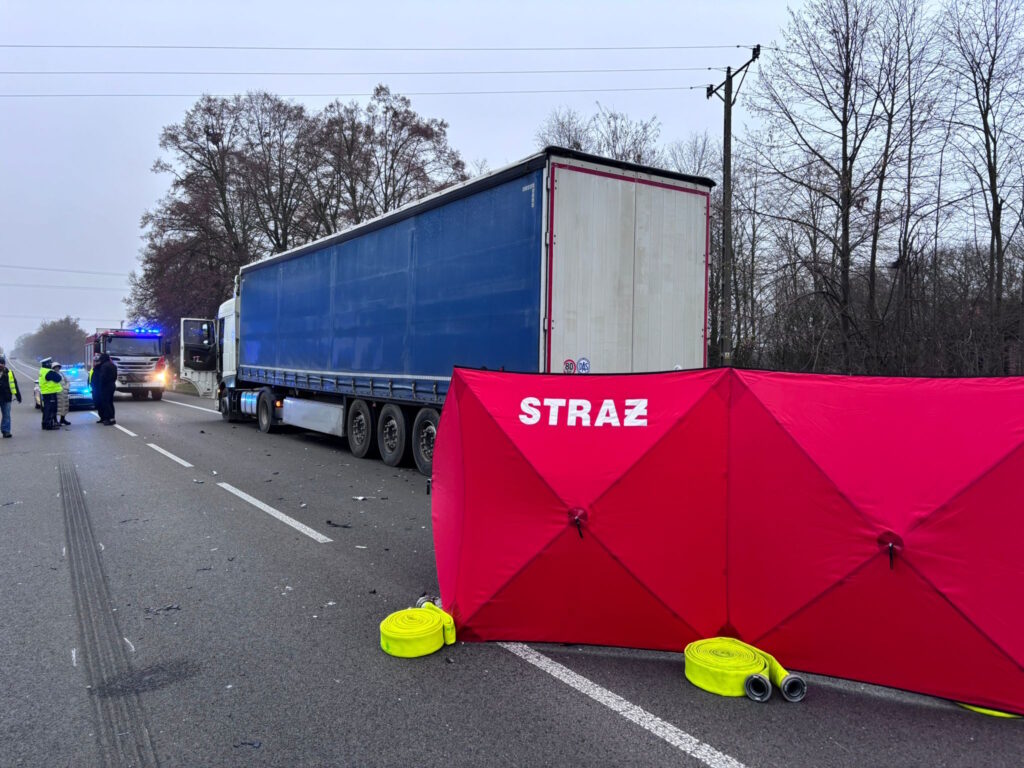 Służby ratunkowe zabezpieczają miejsce wypadku z udziałem ciężarówki, obok widoczny czerwony parawan straży.