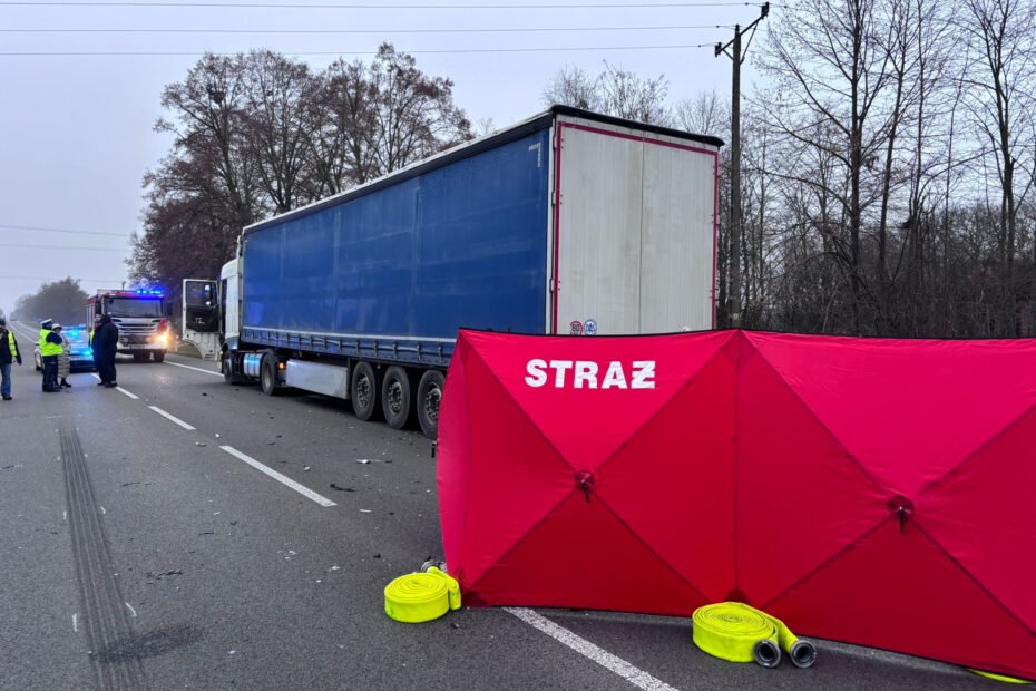 Służby ratunkowe zabezpieczają miejsce wypadku z udziałem ciężarówki, obok widoczny czerwony parawan straży.