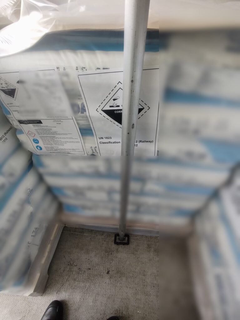 Paczki z oznaczeniem materiału żrącego UN 1823 zabezpieczone w naczepie ciężarówki