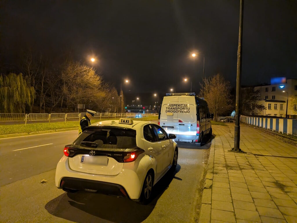 Inspektor podczas nocnej kontroli taksówki, obok pojazd ITD zaparkowany przy drodze.