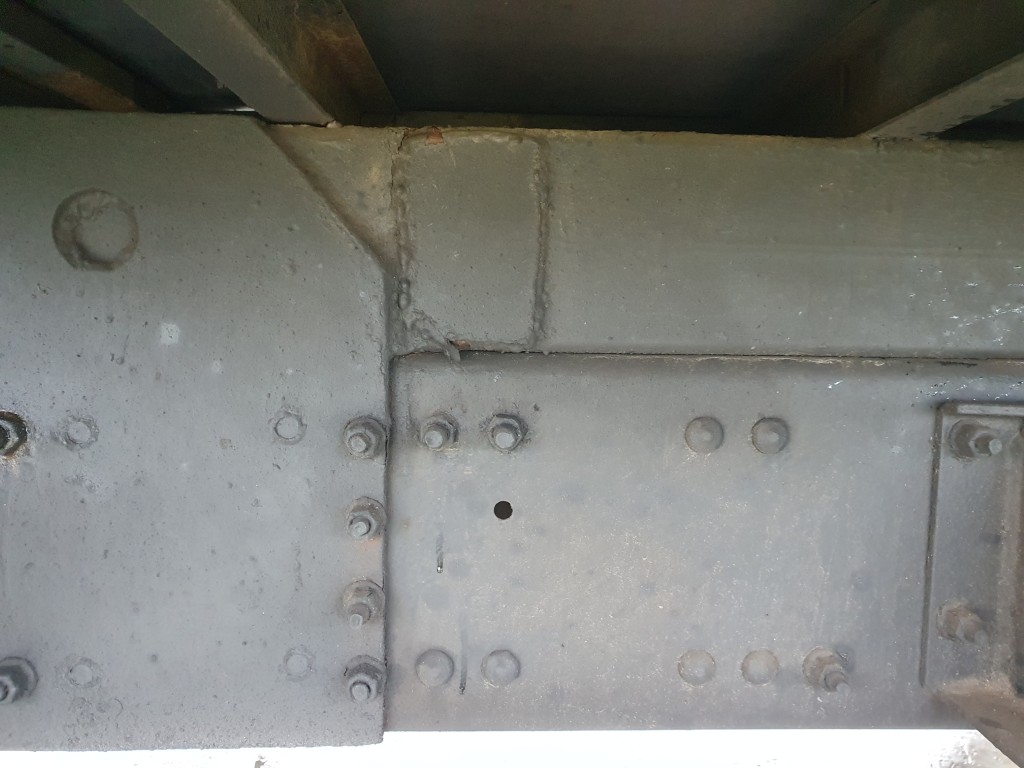 Połączenie śrubowe i spawane ramy pojazdu z widocznymi śladami zużycia i korozji.