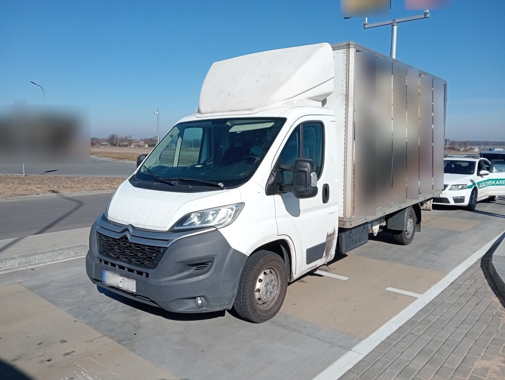 Biały pojazd dostawczy zatrzymany do kontroli na parkingu, obok samochód służb.