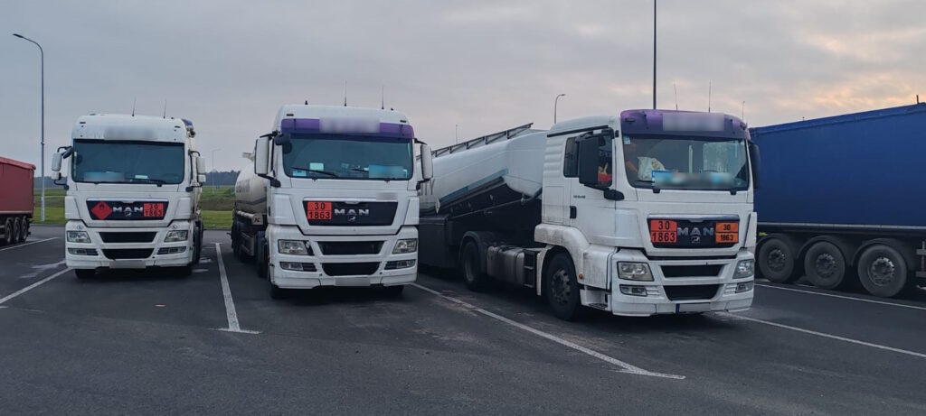 Trzy ciężarówki typu cysterna z oznaczeniami ADR zaparkowane obok siebie na parkingu.