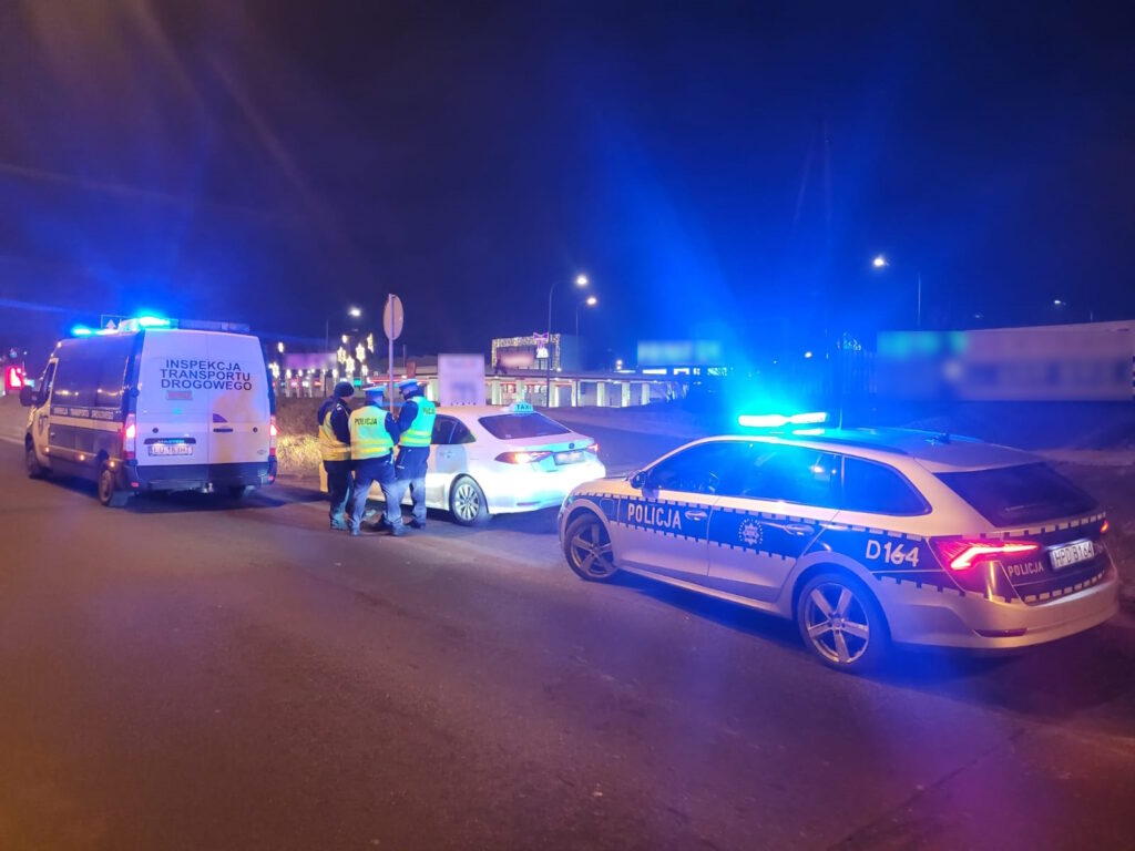 Policja i Inspekcja Transportu Drogowego prowadzą nocną kontrolę taksówki przy drodze.