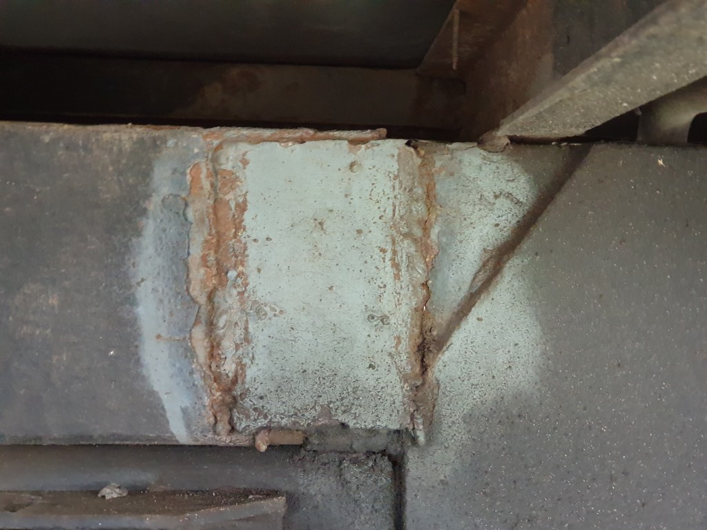 Widoczna korozja i uszkodzenie spawu na stalowym elemencie konstrukcyjnym pojazdu.