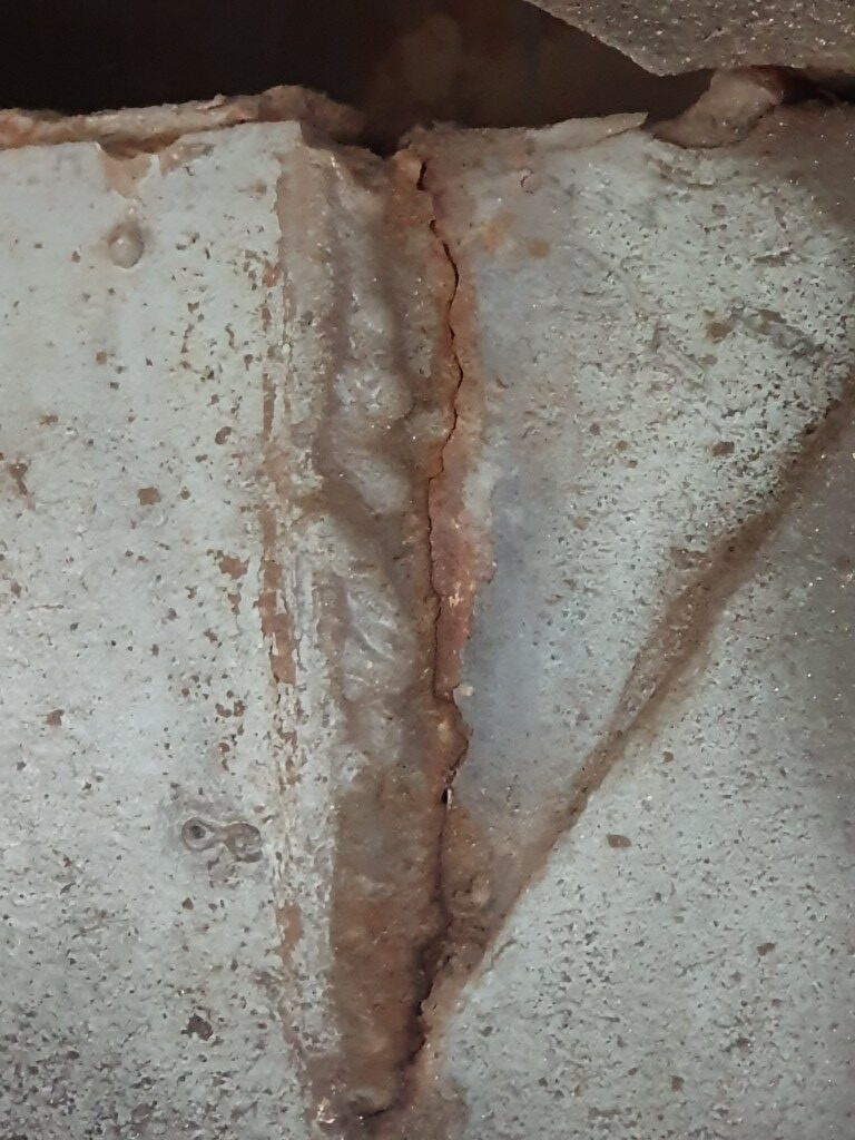 Zbliżenie na skorodowane i pęknięte połączenie spawane elementów stalowej ramy pojazdu.