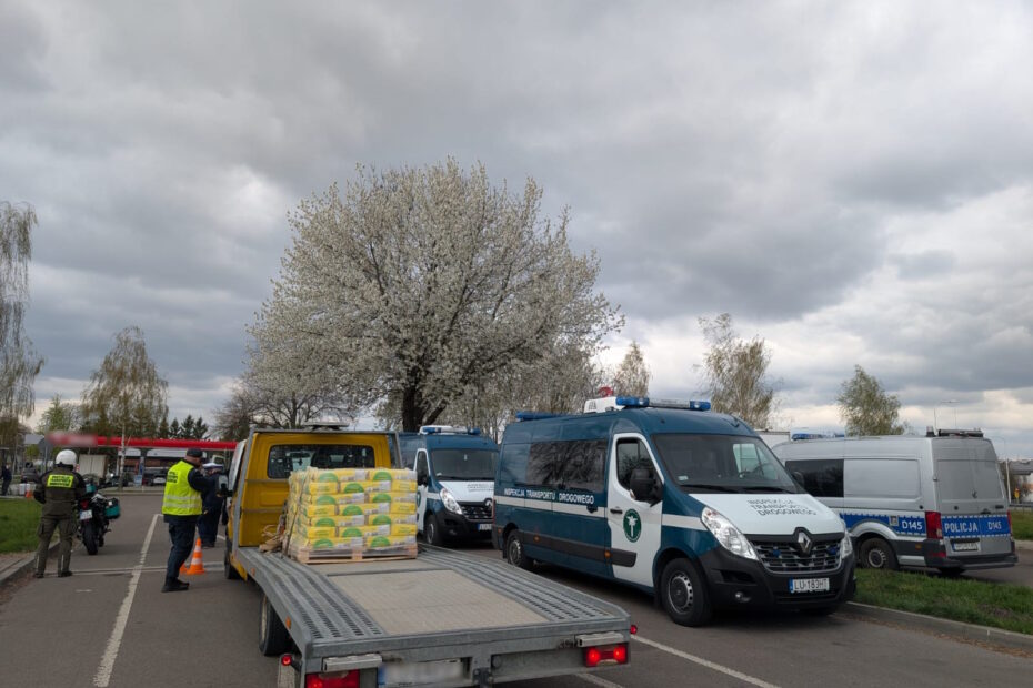 Laweta z ładunkiem materiałów budowlanych podczas kontroli drogowej, w tle pojazdy Inspekcji Transportu Drogowego i policji