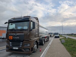 Ciągnik siodłowy z cysterną przewożącą materiały niebezpieczne zatrzymany do kontroli drogowej, w tle pojazd służb kontrolnych