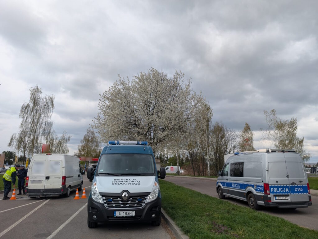 Samochód dostawczy zatrzymany do kontroli drogowej – funkcjonariusze prowadzą czynności przy pojeździe, w pobliżu radiowozy